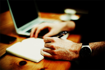 Man's hand, taking notes by a laptop